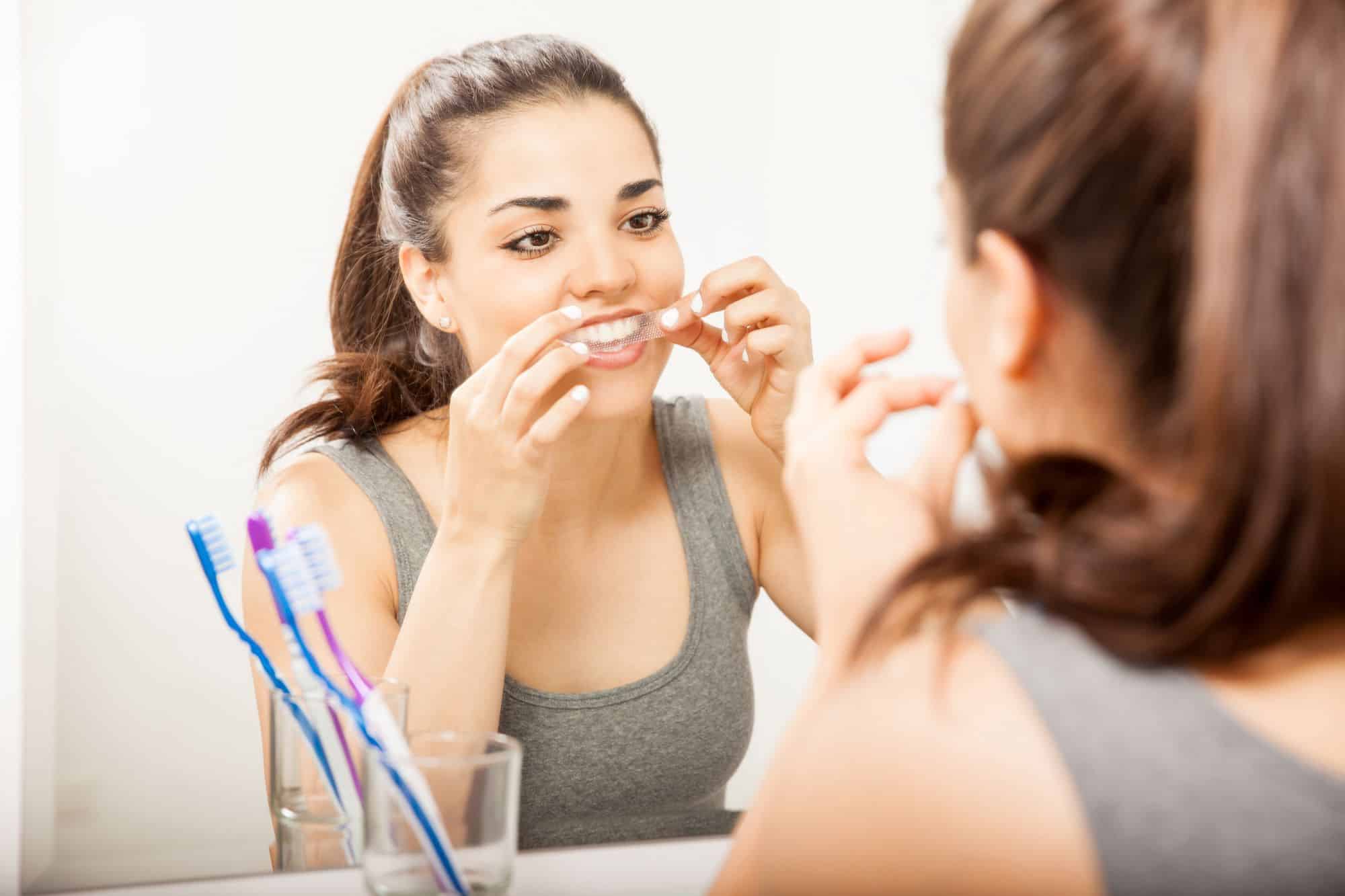 A young woman using a teeth whitening strip (image by AntonioDiaz, Adobe Stock)
